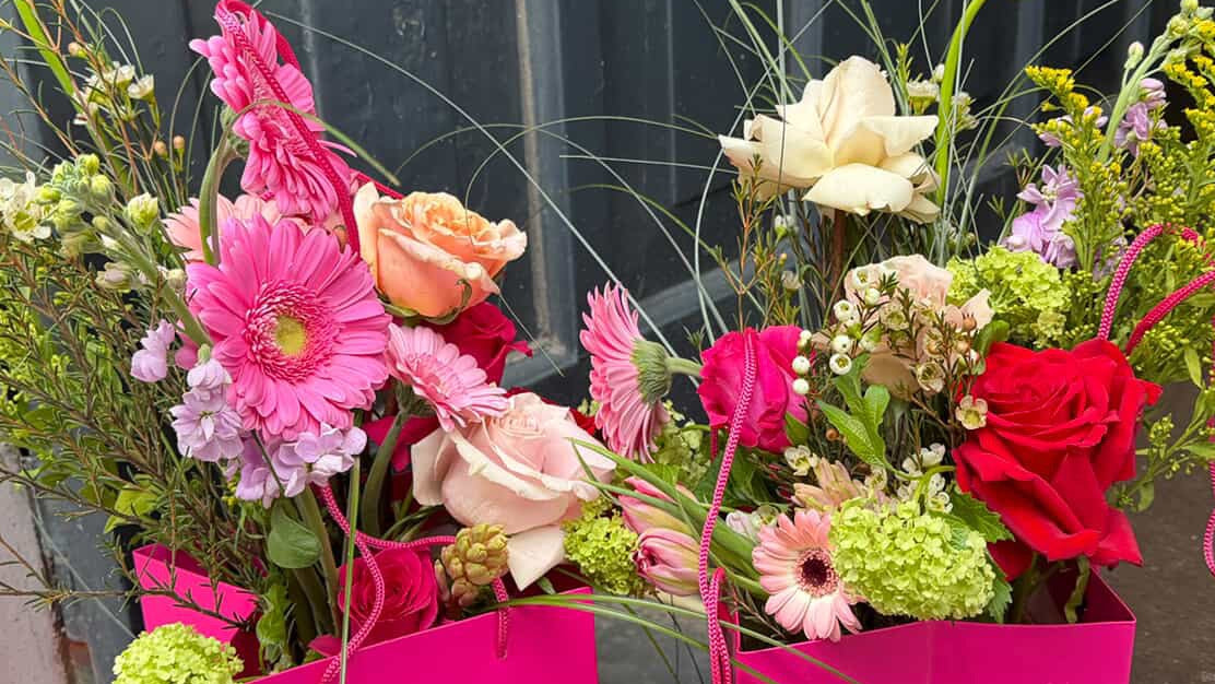 Two vibrant flower arrangements in pink bags against a dark door.